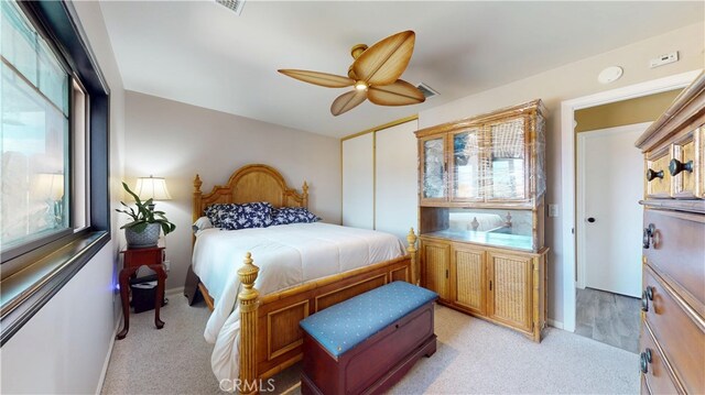 bedroom featuring ceiling fan, visible vents, light carpet, and a closet