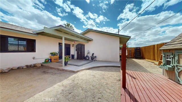 rear view of house featuring fence, a wooden deck, a patio area, and stucco siding