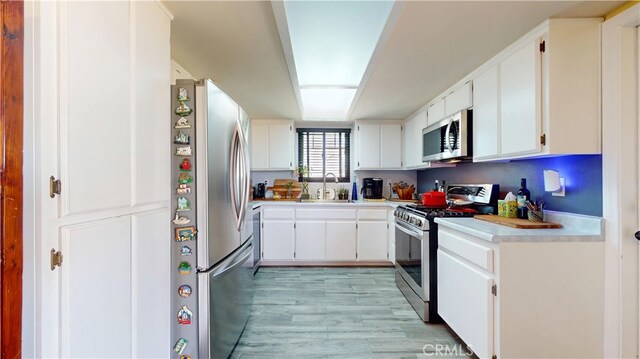 kitchen with light countertops, white cabinets, a sink, light wood finished floors, and stainless steel appliances