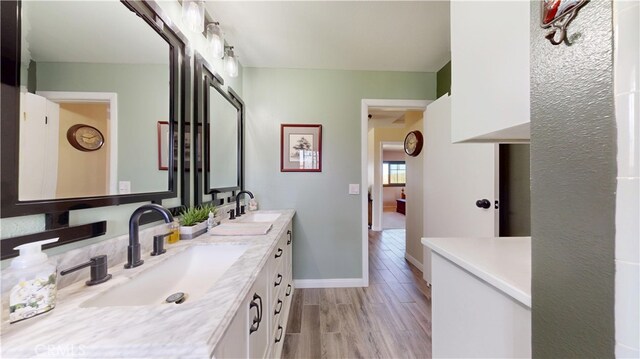 bathroom featuring double vanity, baseboards, a sink, and wood finished floors