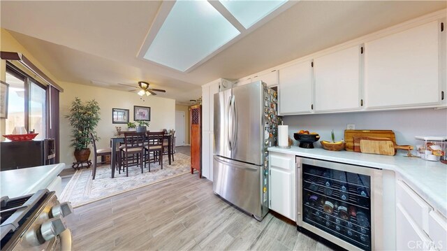 kitchen with beverage cooler, light countertops, white cabinets, light wood-style flooring, and stainless steel appliances