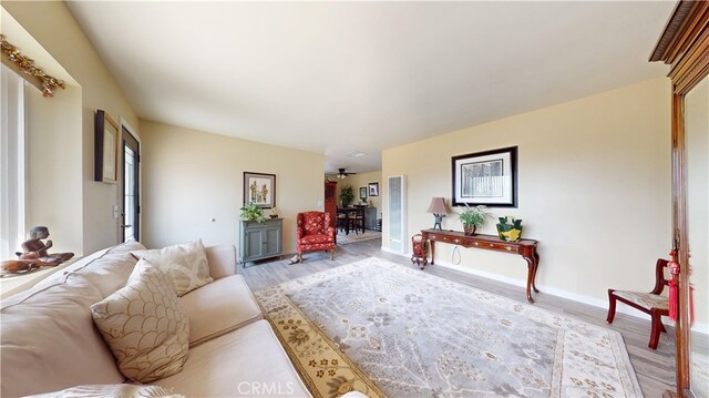 living area featuring baseboards, ceiling fan, and light wood finished floors