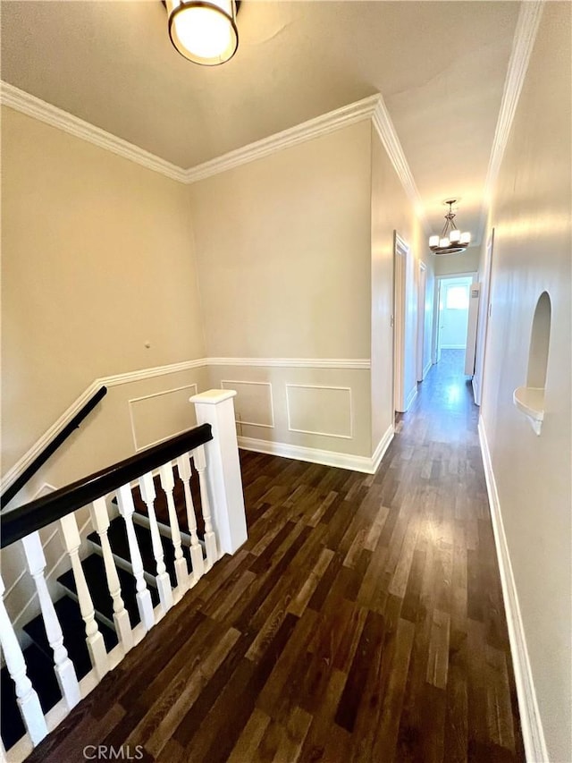 hallway with ornamental molding, dark wood-style flooring, a notable chandelier, and an upstairs landing