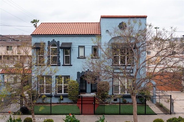 mediterranean / spanish home with a gate, stucco siding, a fenced front yard, and a tiled roof