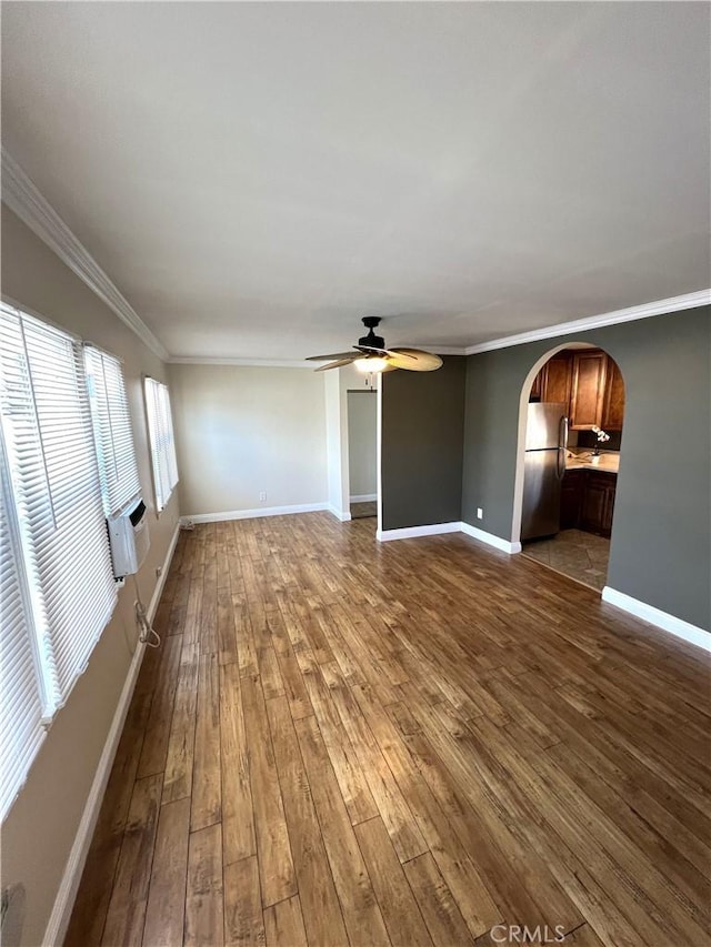 unfurnished living room featuring crown molding, baseboards, dark wood-style floors, arched walkways, and a ceiling fan