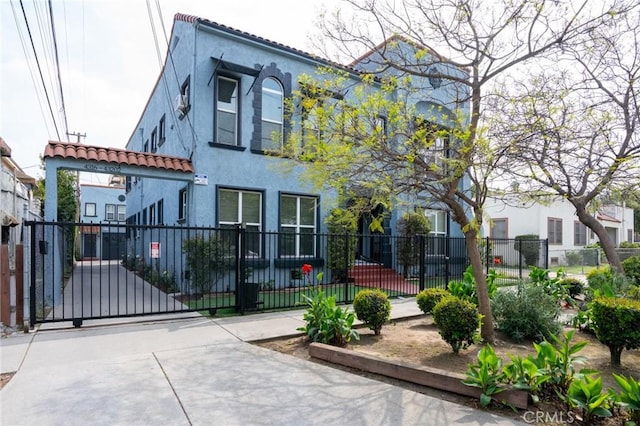 exterior space featuring a tiled roof, a gate, stucco siding, and a fenced front yard