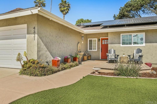 doorway to property with an attached garage, stucco siding, a deck, solar panels, and a lawn