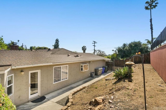 back of property with a fenced backyard, roof with shingles, stucco siding, and a chimney