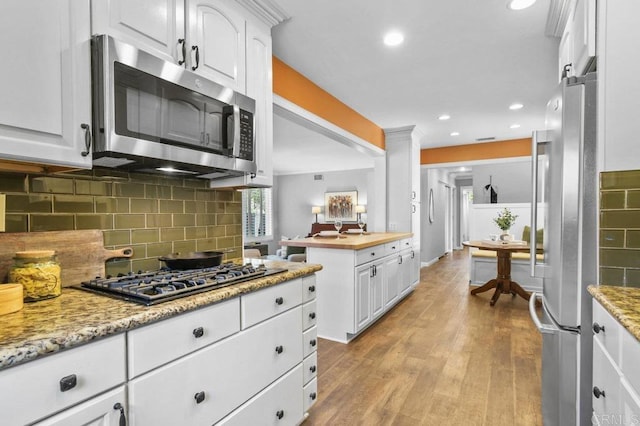 kitchen with light wood-style floors, appliances with stainless steel finishes, white cabinets, and backsplash