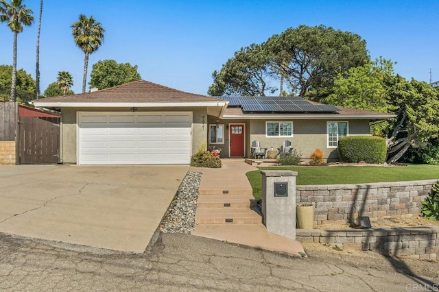 ranch-style house with concrete driveway, an attached garage, solar panels, and stucco siding