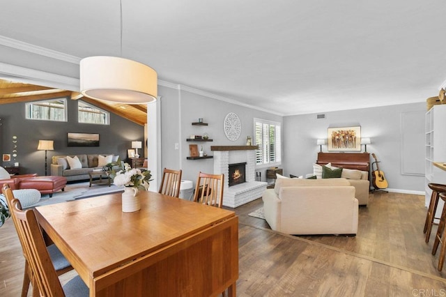 dining area featuring crown molding, visible vents, a brick fireplace, wood finished floors, and lofted ceiling