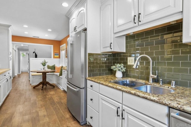 kitchen with a sink, stainless steel appliances, white cabinetry, wood finished floors, and backsplash