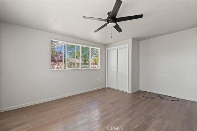 unfurnished bedroom featuring baseboards, a ceiling fan, wood finished floors, and a closet