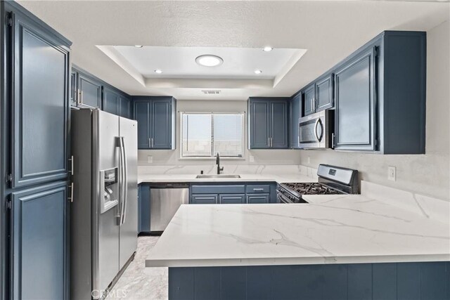 kitchen with light stone counters, a sink, stainless steel appliances, a peninsula, and a tray ceiling