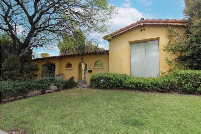 mediterranean / spanish home featuring a tiled roof, stucco siding, and a front lawn