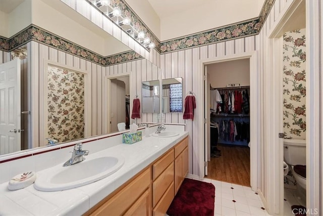 full bathroom with a sink, toilet, wallpapered walls, and double vanity