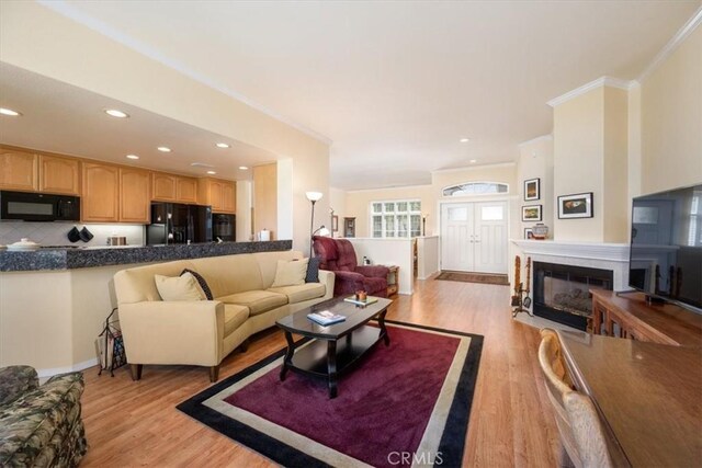 living room with recessed lighting, a glass covered fireplace, ornamental molding, and light wood-type flooring