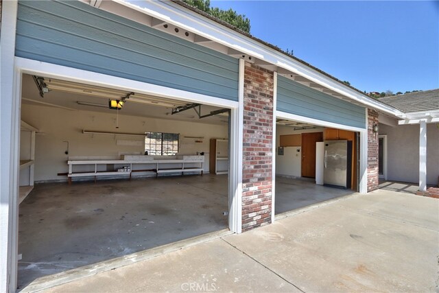garage with concrete driveway, a garage door opener, and freestanding refrigerator