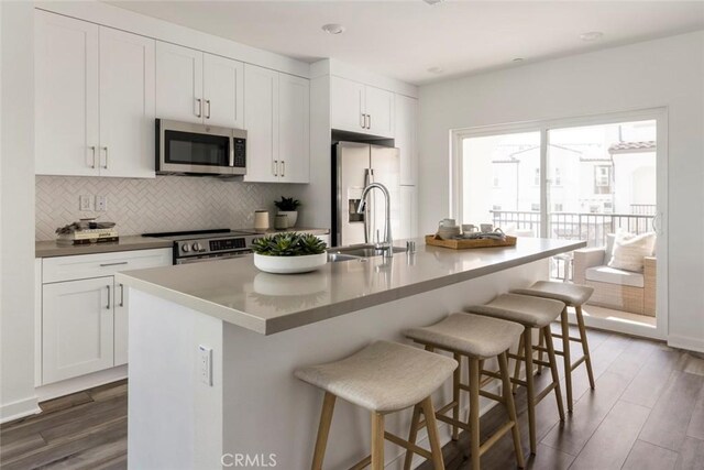 kitchen with stainless steel appliances, decorative backsplash, an island with sink, and dark wood-type flooring