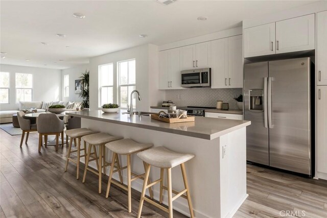 kitchen with appliances with stainless steel finishes, a kitchen breakfast bar, open floor plan, light wood-type flooring, and backsplash