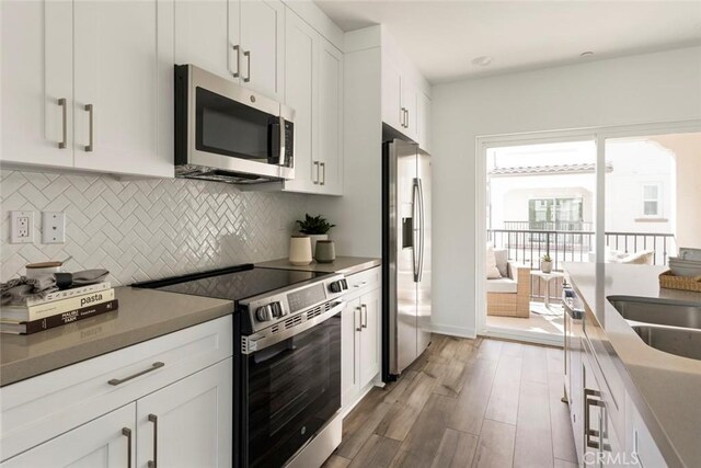 kitchen featuring light wood-style floors, white cabinetry, tasteful backsplash, a sink, and stainless steel appliances