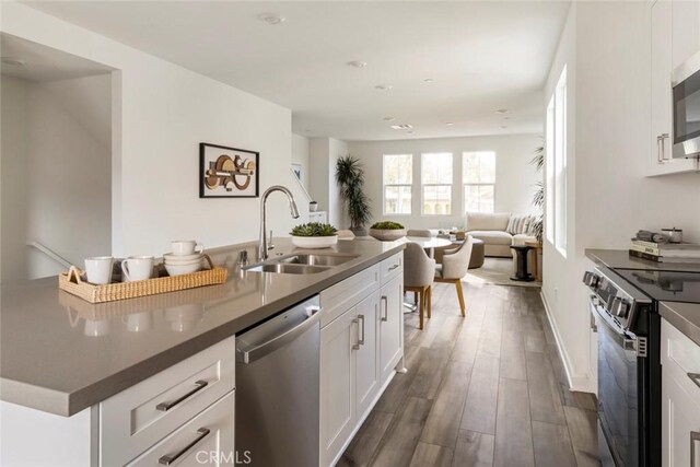 kitchen with a sink, stainless steel appliances, open floor plan, white cabinetry, and dark wood-type flooring