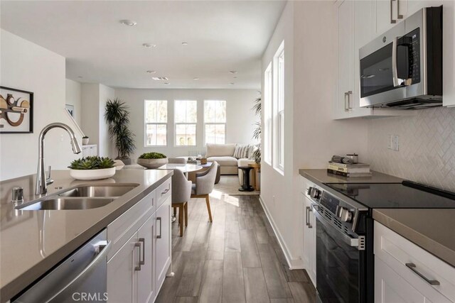 kitchen featuring appliances with stainless steel finishes, a sink, white cabinetry, decorative backsplash, and dark wood-type flooring