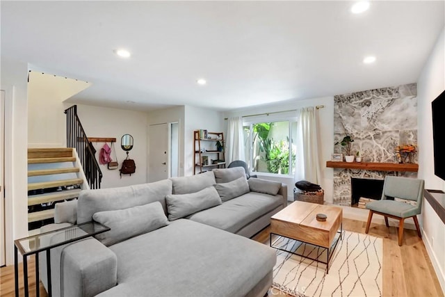 living area with stairway, recessed lighting, light wood finished floors, and a stone fireplace