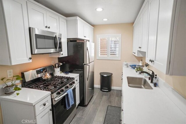 kitchen with baseboards, white cabinets, a sink, light wood-style flooring, and appliances with stainless steel finishes