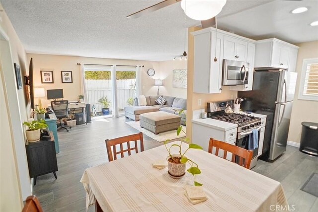 kitchen with a textured ceiling, light wood-style flooring, stainless steel appliances, and white cabinetry