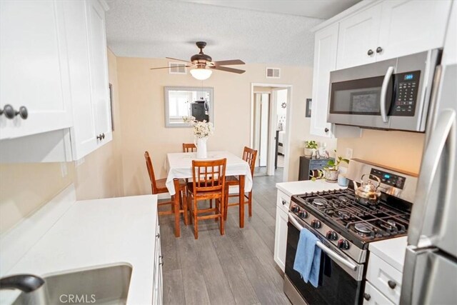 kitchen with wood finished floors, ceiling fan, light countertops, white cabinetry, and appliances with stainless steel finishes