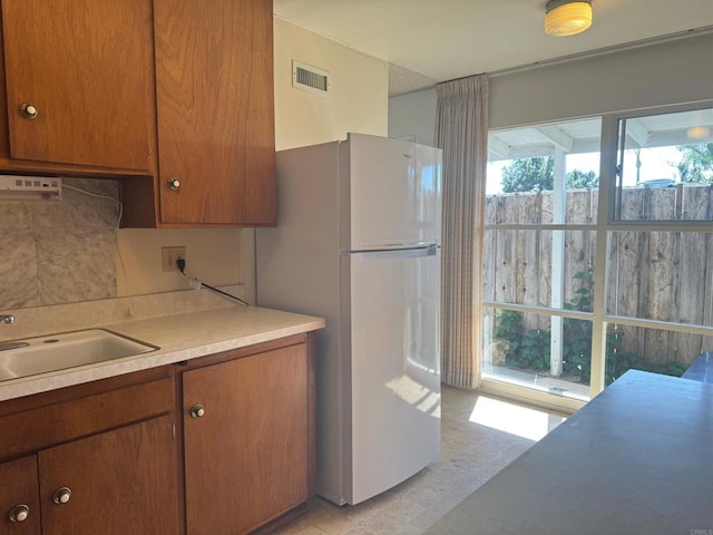 kitchen with visible vents, freestanding refrigerator, brown cabinetry, light countertops, and a sink