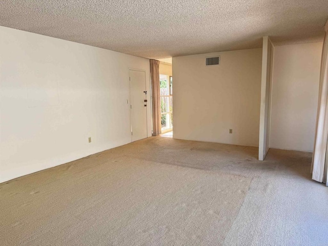 spare room featuring light carpet, a textured ceiling, and visible vents