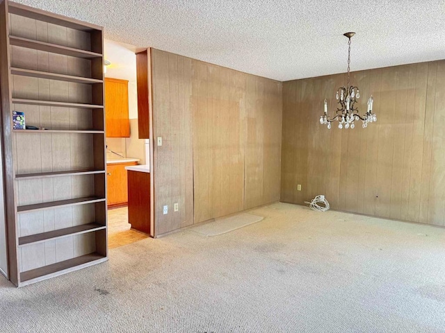 unfurnished dining area featuring carpet floors, wooden walls, a textured ceiling, and a notable chandelier