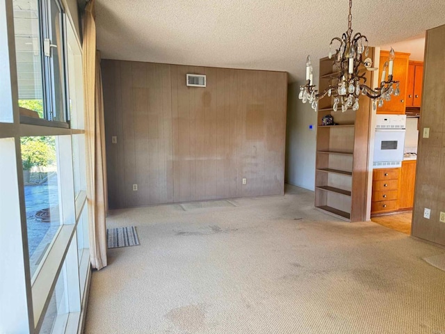 unfurnished dining area featuring an inviting chandelier, carpet flooring, a textured ceiling, and visible vents