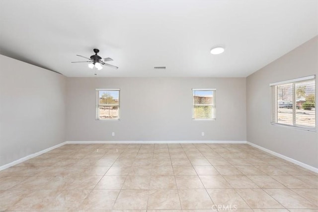 empty room with baseboards, ceiling fan, visible vents, and a wealth of natural light