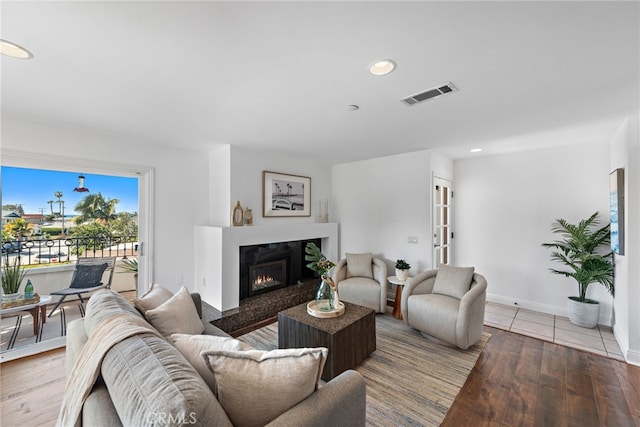 living room with a glass covered fireplace, recessed lighting, baseboards, wood finished floors, and visible vents