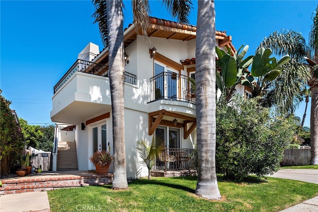 view of front facade featuring french doors, stucco siding, a balcony, and fence