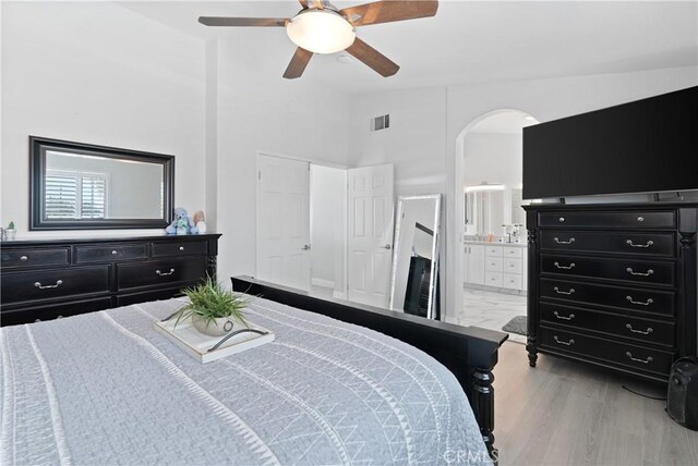 bedroom featuring ceiling fan, arched walkways, ensuite bathroom, wood finished floors, and visible vents