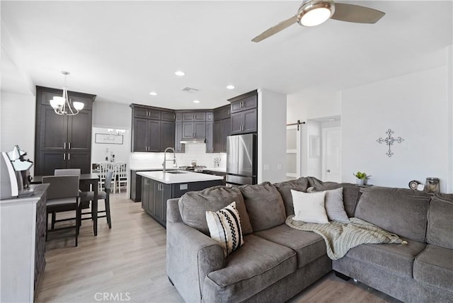 living area with light wood-type flooring, recessed lighting, and ceiling fan with notable chandelier