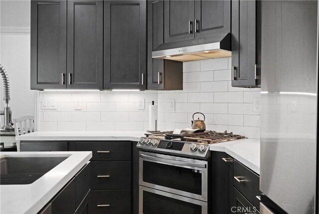 kitchen with light countertops, under cabinet range hood, tasteful backsplash, a sink, and stainless steel appliances