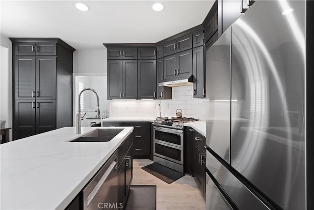 kitchen with decorative backsplash, appliances with stainless steel finishes, a sink, light wood-style floors, and under cabinet range hood