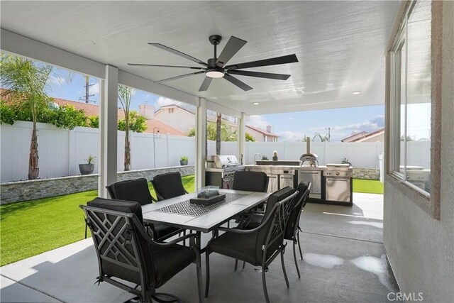 view of patio featuring an outdoor kitchen, outdoor dining area, ceiling fan, and a fenced backyard