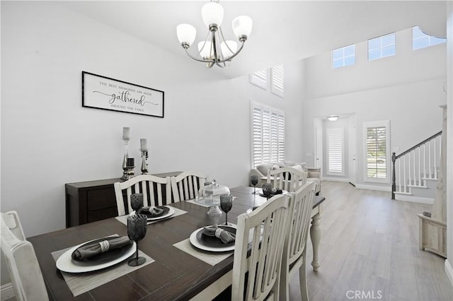 dining area featuring stairs, a chandelier, light wood finished floors, and a towering ceiling