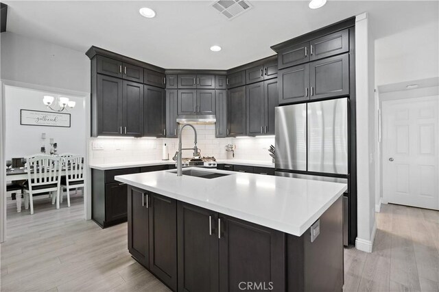 kitchen featuring a sink, light countertops, light wood-style flooring, decorative backsplash, and visible vents
