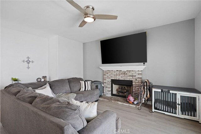 living area featuring ceiling fan, a fireplace, and wood finished floors