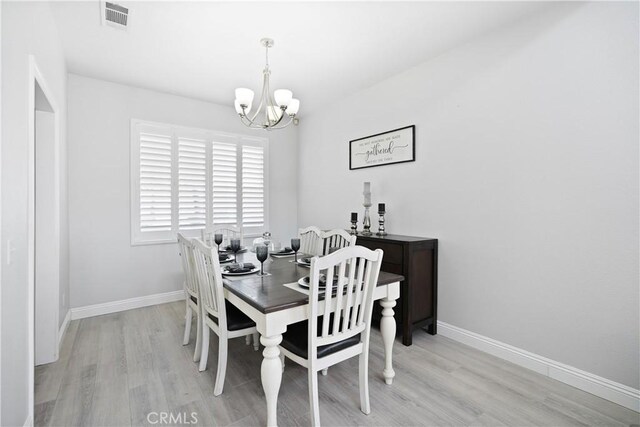 dining area featuring baseboards, visible vents, light wood finished floors, and a chandelier