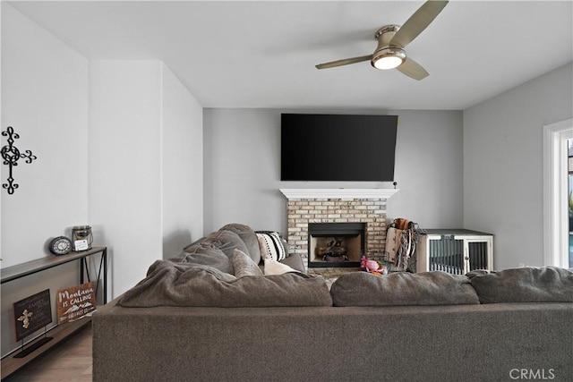 living room featuring ceiling fan, a brick fireplace, and wood finished floors