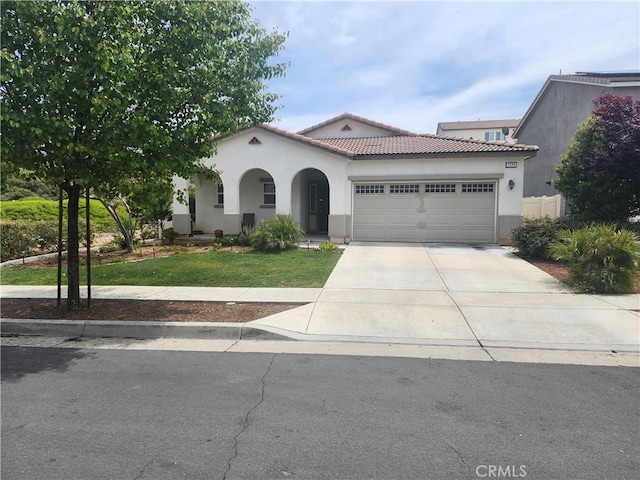 mediterranean / spanish home with a garage, a front lawn, stucco siding, driveway, and a tile roof