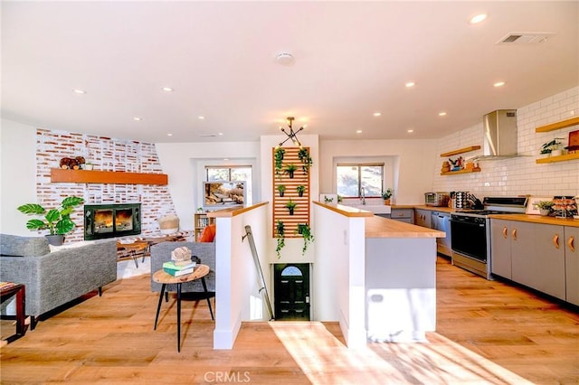 kitchen with wall chimney range hood, a brick fireplace, range, butcher block countertops, and visible vents